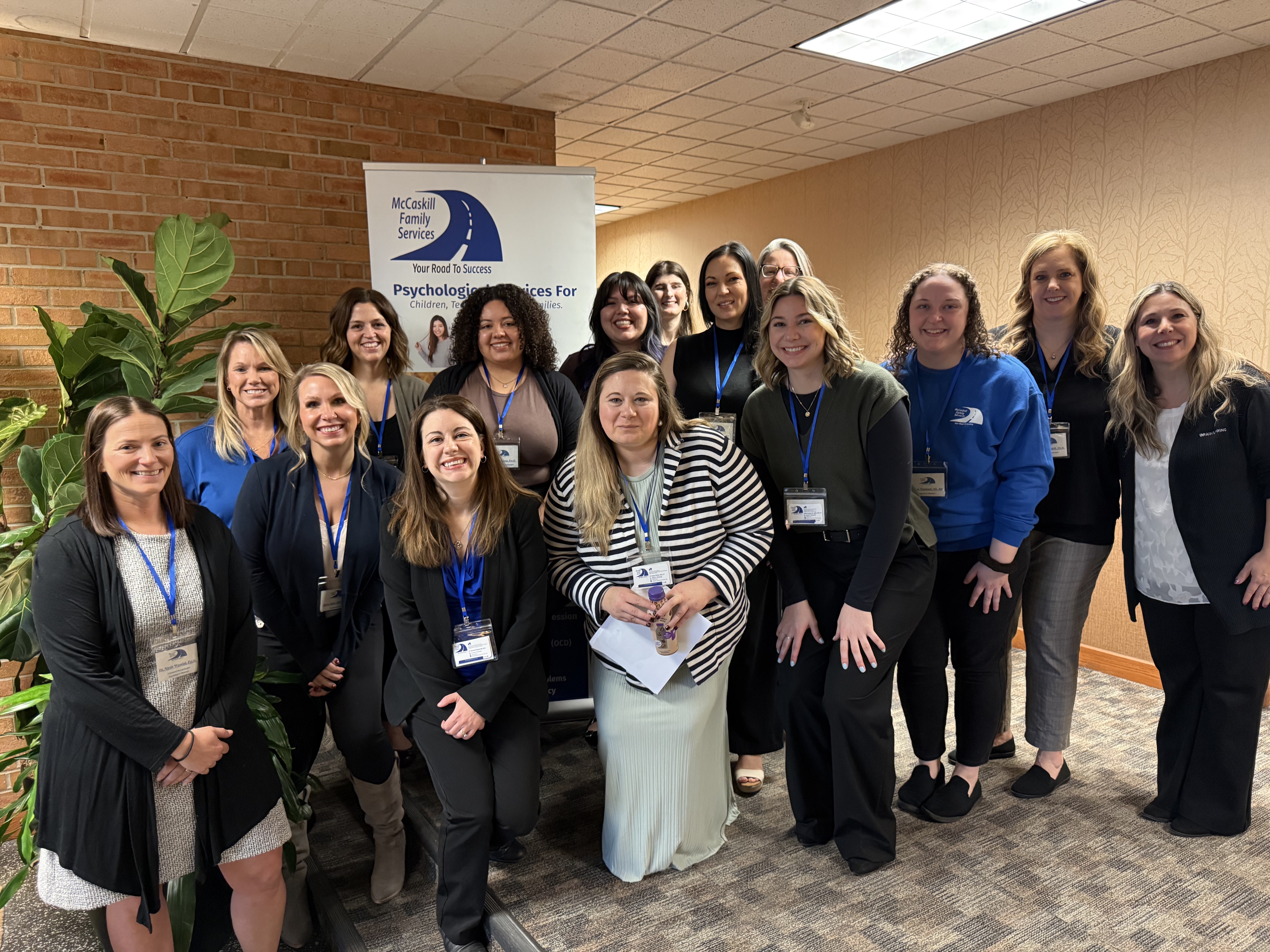 Group photo of a team from McCaskill Family Services, standing together in a conference setting, with a banner in the background promoting psychological services.