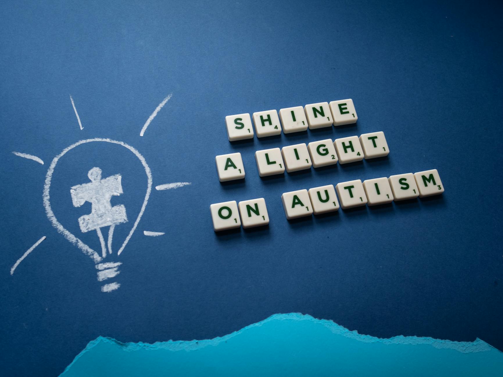 a slogan on autism spelled on scrabble tiles with a light bulb drawing